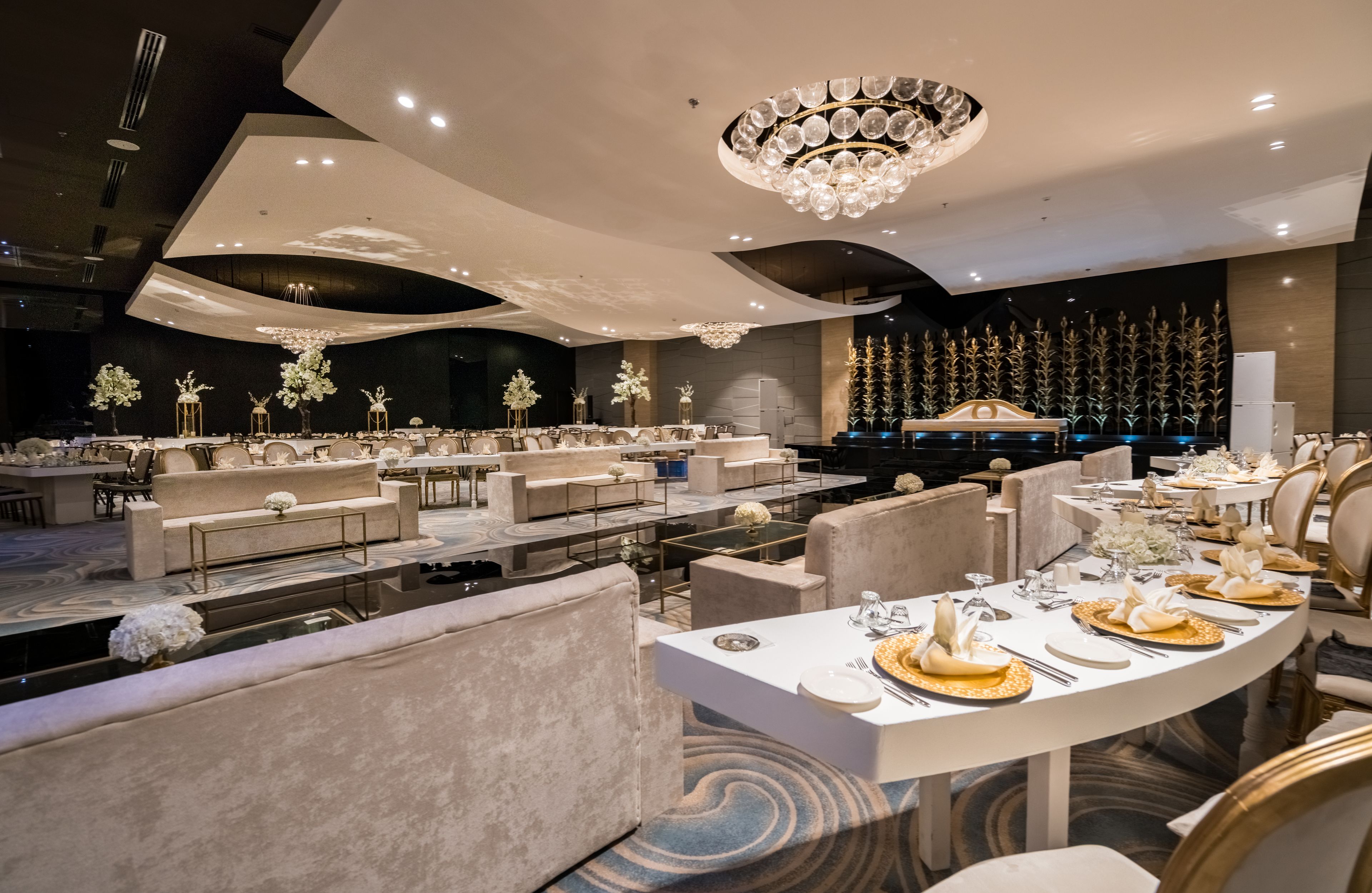 A modern dining area with round tables, plush seating, and elegant chandeliers.