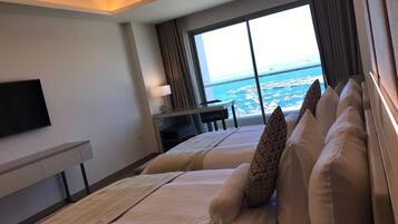 Quarto de hotel com uma cama grande, uma escrivaninha, televisão e vista para o mar.