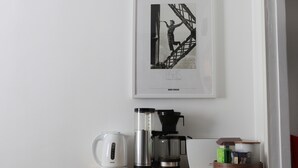 A framed black and white photograph of a person climbing a ladder, with the word "PARIS" and "MARC RIBOUDET" below it. Below the photo, there is a coffee maker, a kettle, and a basket with books and a box.