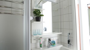 Un baño con lavamanos blanco, un espejo, una repisa con planta en maceta y zona de ducha.
