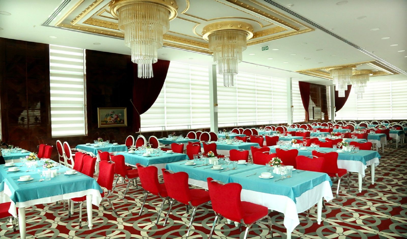 A banquet hall with rows of tables, red chairs, and blue tablecloths.