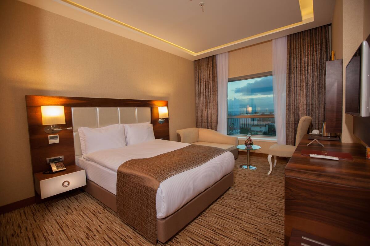 A hotel room with a large bed, a desk, a chair, a small table, and a TV.