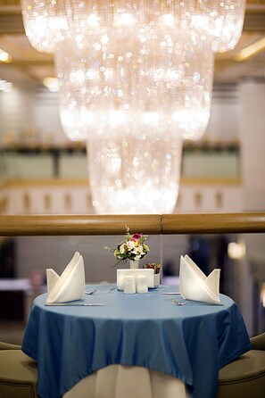 A table with a blue tablecloth, two folded white napkins, a small vase with flowers, and salt and pepper shakers. - Mitannia Regency Hotel (Diyarbakir)