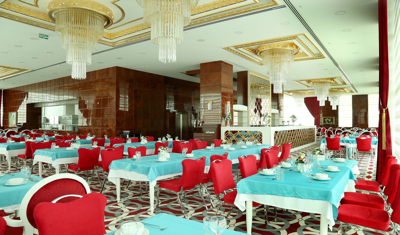 A banquet hall with multiple tables set for dining, red chairs, and chandeliers.