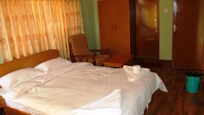 A bedroom with a large bed, a wooden wardrobe, a chair, and a trash bin. - Hotel Green Orchid (Kathmandu)