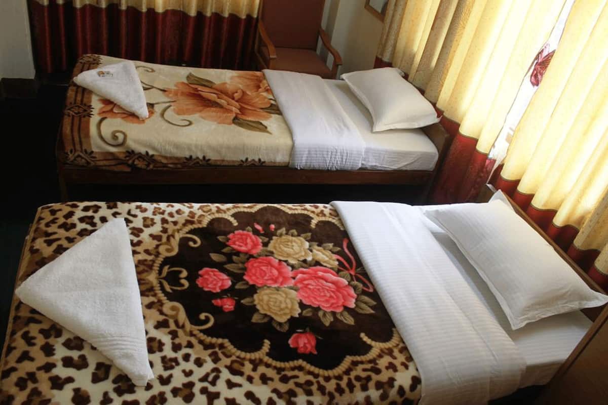 Two beds with floral and leopard print bedspreads, white pillows, and a small white towel on each bed.