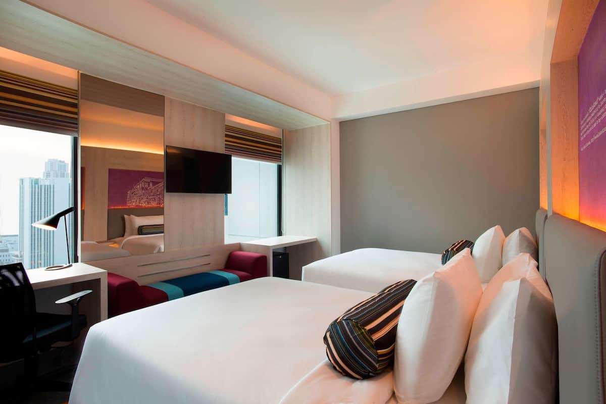 A modern hotel room with a large bed, a desk, and a seating area with a view of the city.
