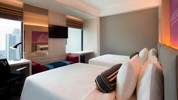 A modern hotel room with a large bed, a desk, and a seating area with a view of the city.
