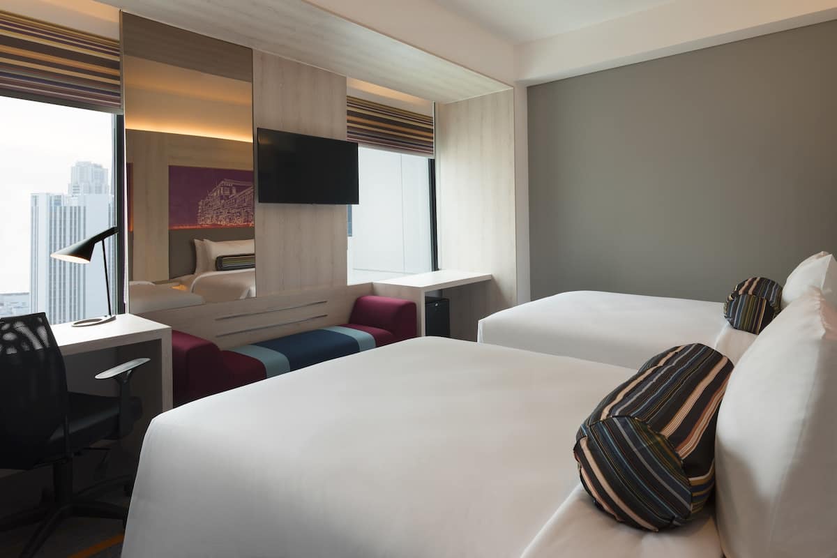 Ein Hotelzimmer mit Bett, Schreibtisch, Stuhl, Fernseher und Fenster mit Blick auf die Stadt.