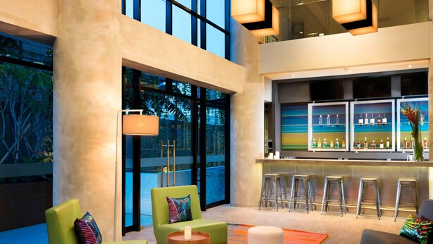 Eine moderne Lobby mit grünen Sitzgelegenheiten, einer Bar und großen Fenstern.