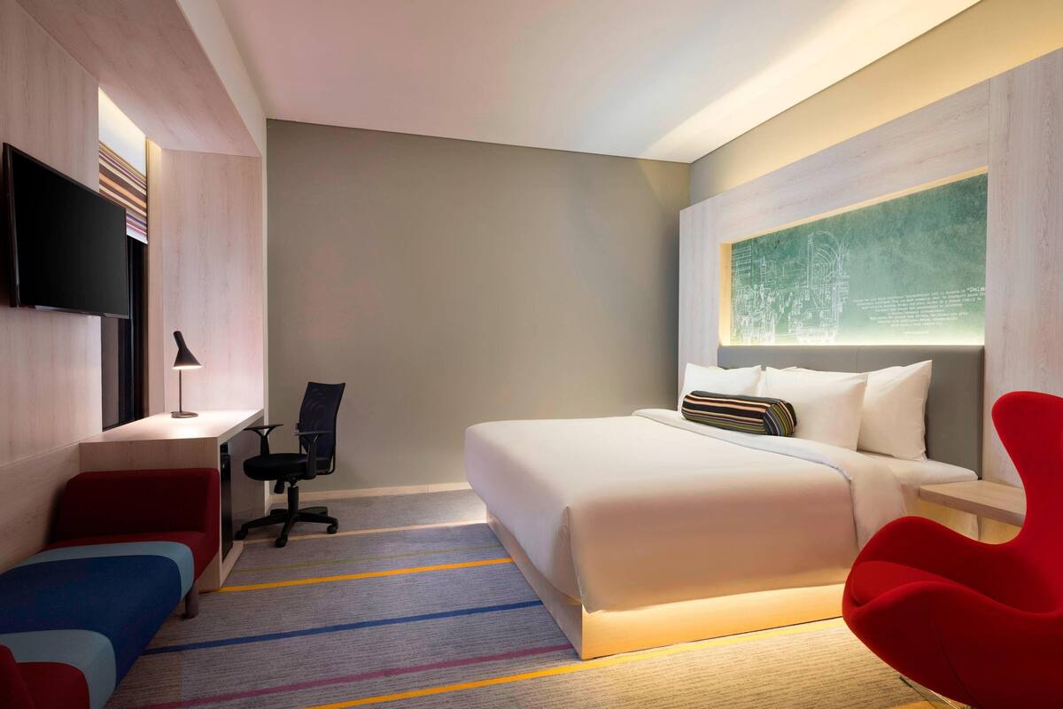 A modern hotel room with a large bed, a desk, a chair, and a TV.