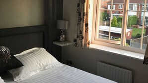 A bedroom with a bed, a nightstand, a lamp, and a window with curtains. - York Holiday Home (York)