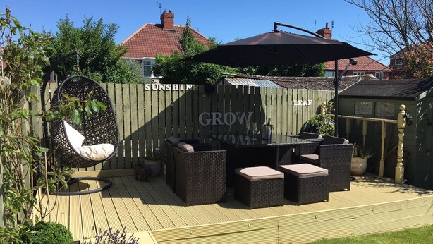 An outdoor patio with a wooden deck, wicker furniture, and a hanging chair. - York Holiday Home (York)