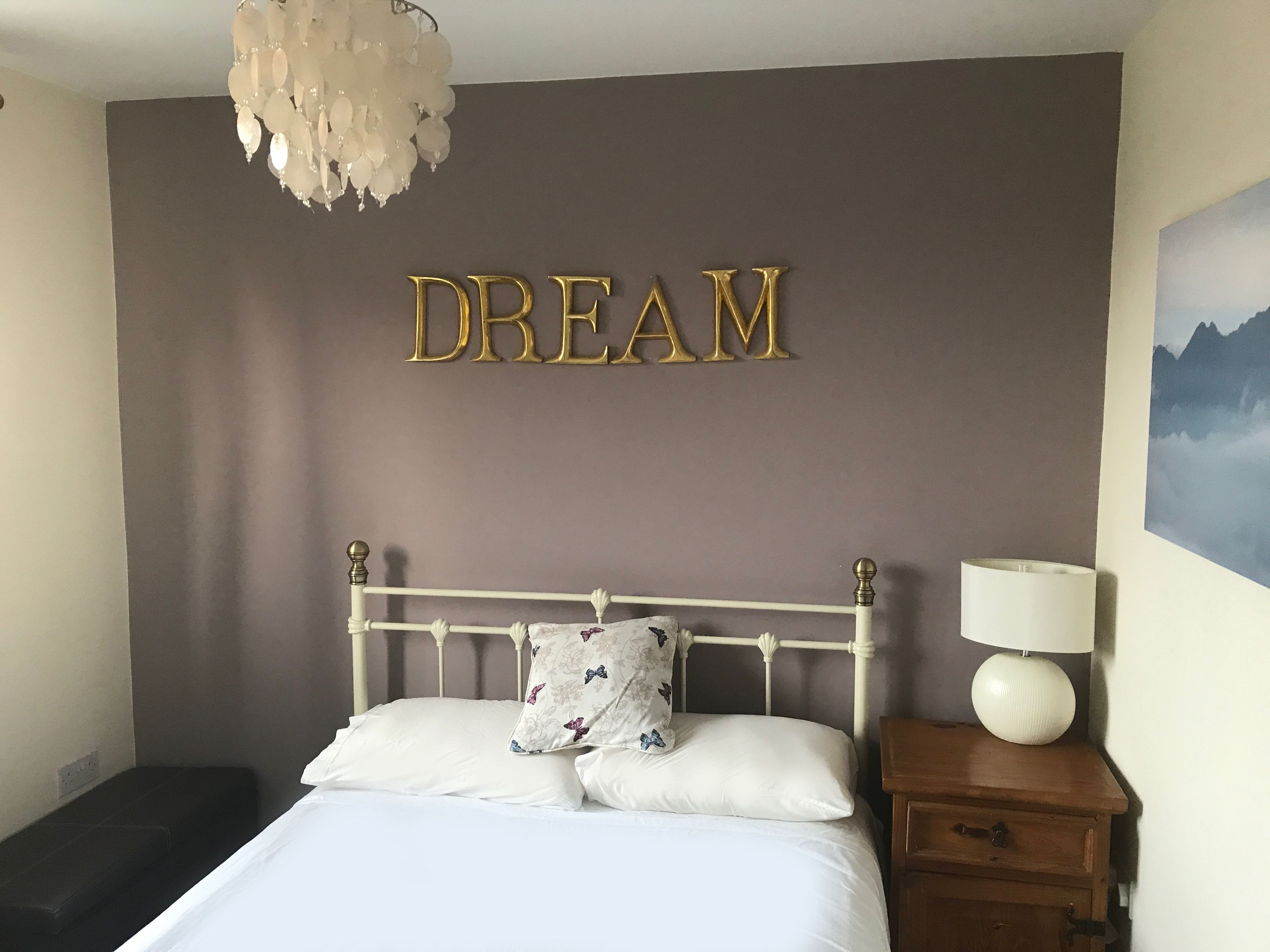 A bedroom with a bed, a nightstand with a lamp, a wall-mounted chandelier, and a 'DREAM' sign.