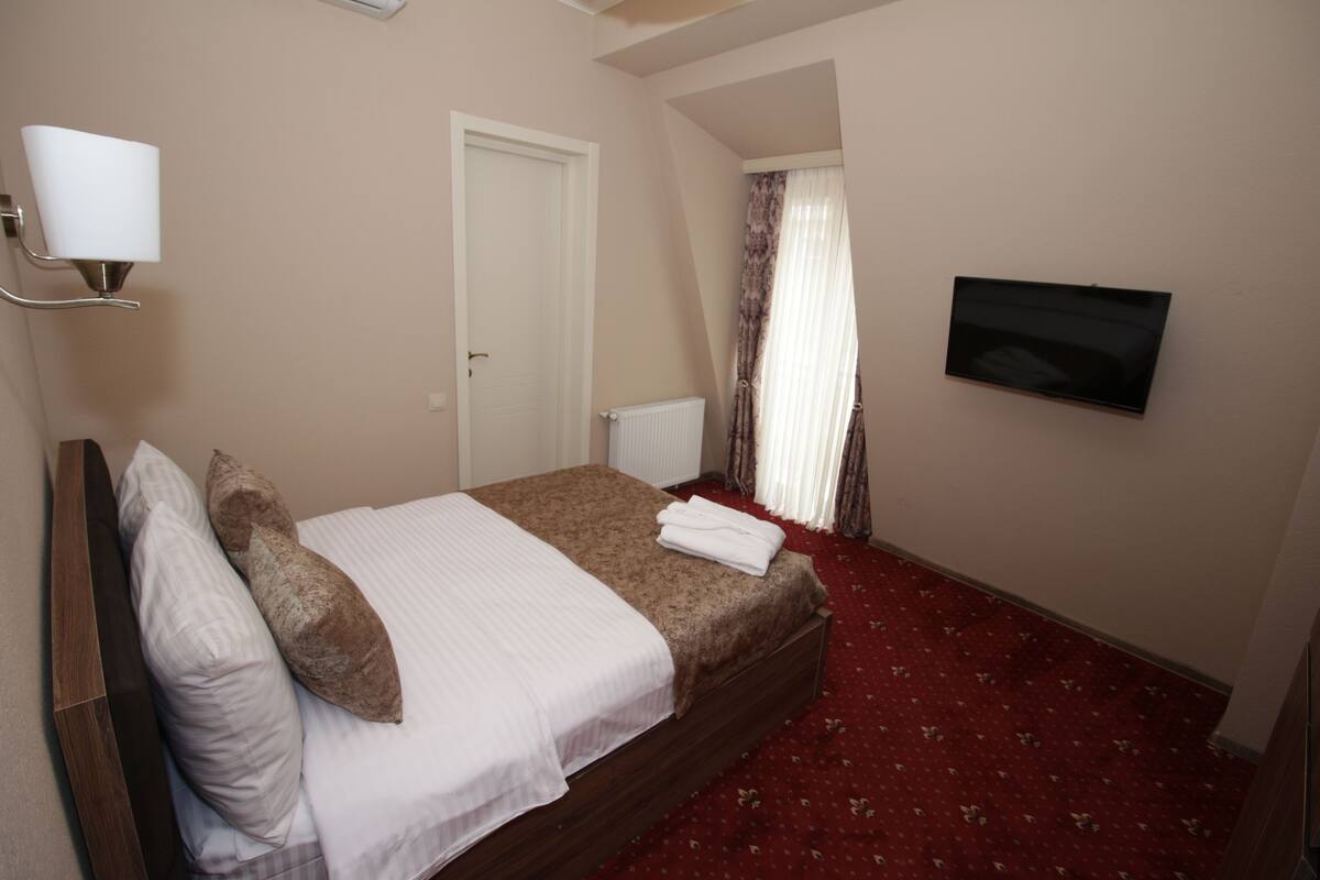 A hotel room with a bed, a TV mounted on the wall, and a red carpeted floor.