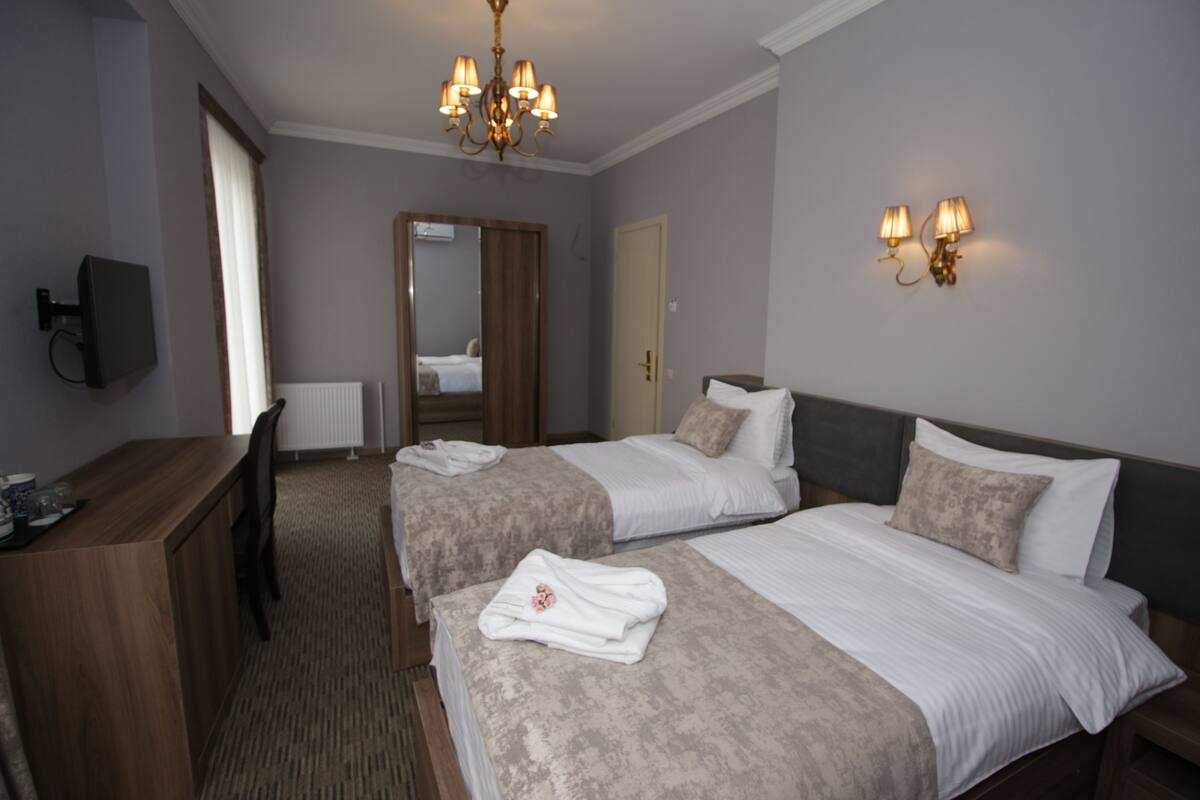 A hotel room with two beds, a wooden desk, a mirror, and a chandelier.