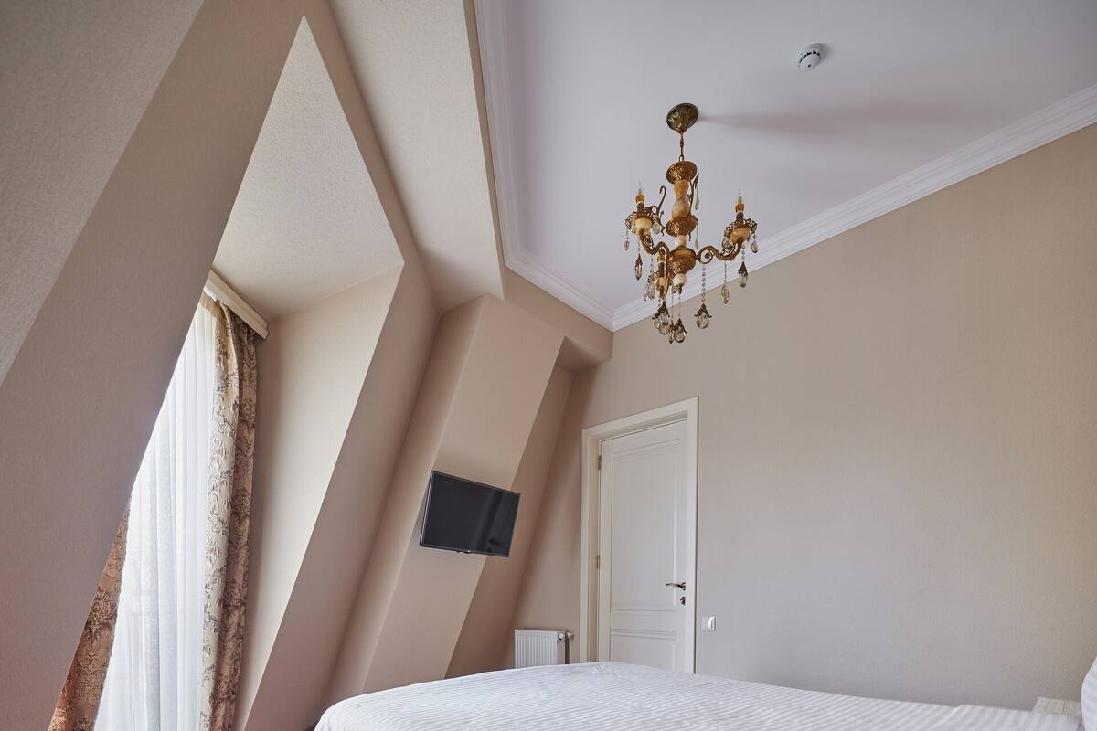 A bedroom with a large bed, a chandelier, a flat-screen TV, and a window with curtains.