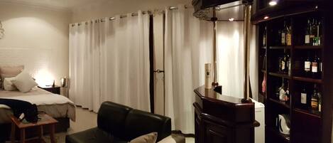 A hotel room with a bed, bedside tables, a desk, a chair, a wardrobe, and a minibar.