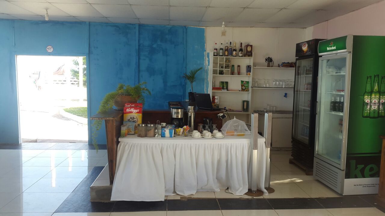 A small cafe with a table set for two, a refrigerator stocked with beverages, and a shelf with various items.