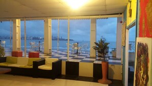 Una terraza con suelo a cuadros, zona de estar y amplios ventanales con vistas al agua.