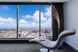 A modern hotel room with a large window offering a city view, a contemporary chair, and a magazine on the windowsill.