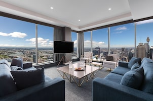 A modern living room with a city view, a flat-screen TV, and a dining area with a table set for two.