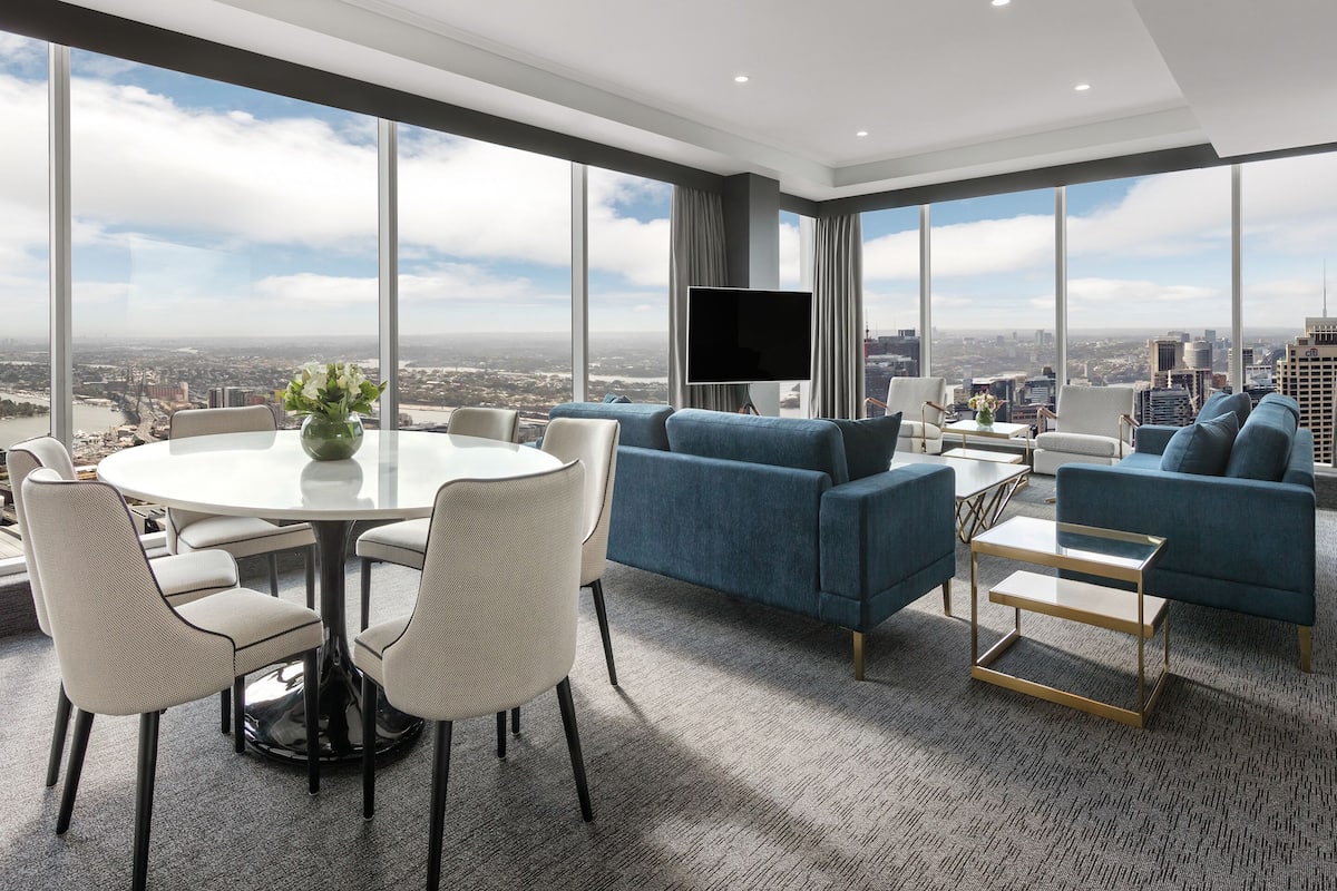 A modern living room with a city view, a round dining table with chairs, and a blue sofa.