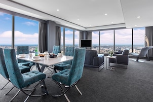 A modern hotel room with a dining area, a flat-screen TV, and a city view.