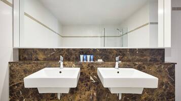 A bathroom with two white sinks, a marble backsplash, and a glass shower enclosure.