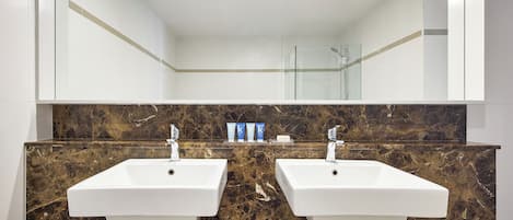 Un baño con dos lavamanos blancos, salpicadero de mármol y cabina de ducha de vidrio.