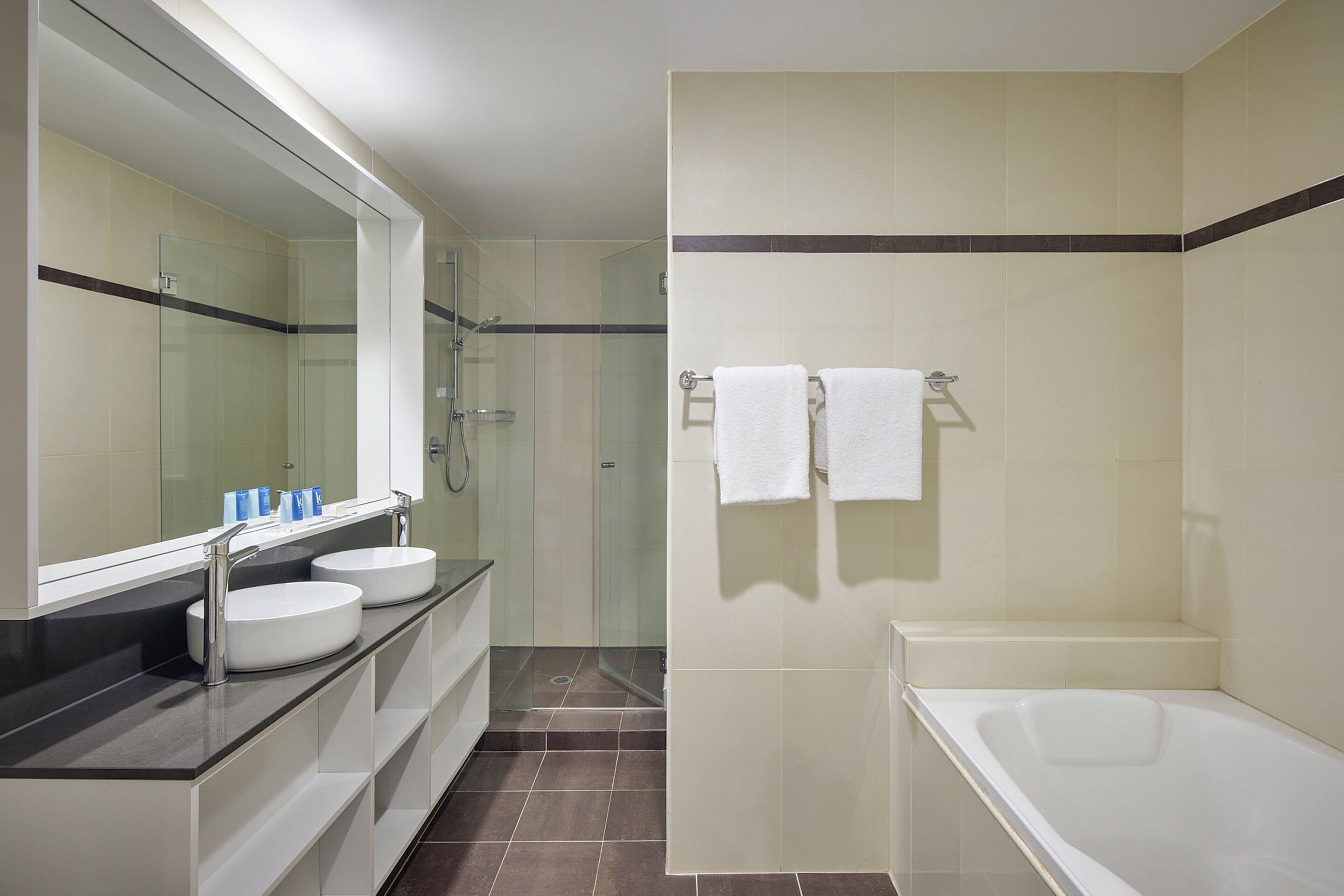 Une salle de bain moderne avec un grand miroir, deux lavabos, une baignoire et une douche à l’italienne.