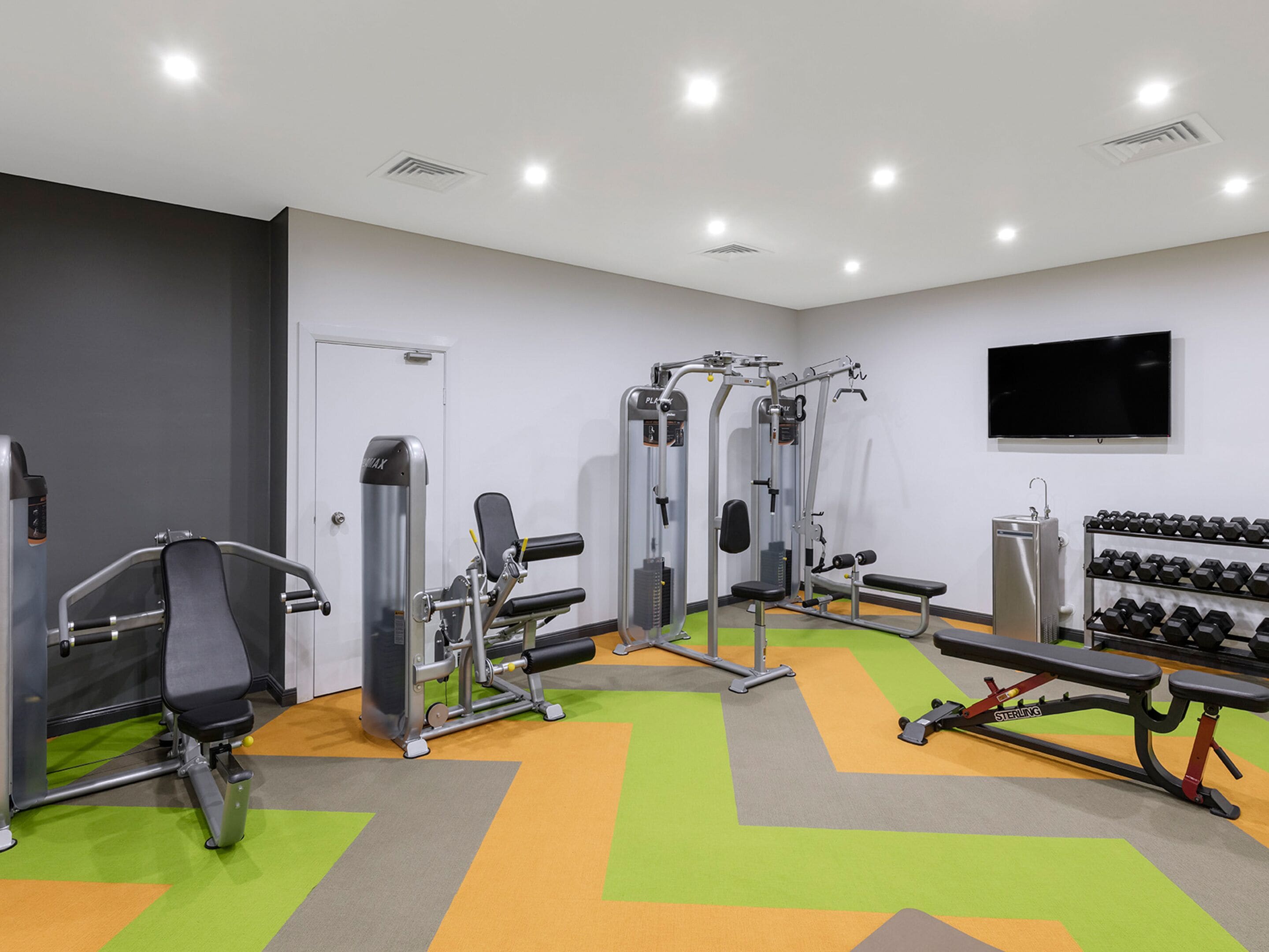 A gym with various exercise machines, a bench, and a rack of dumbbells.