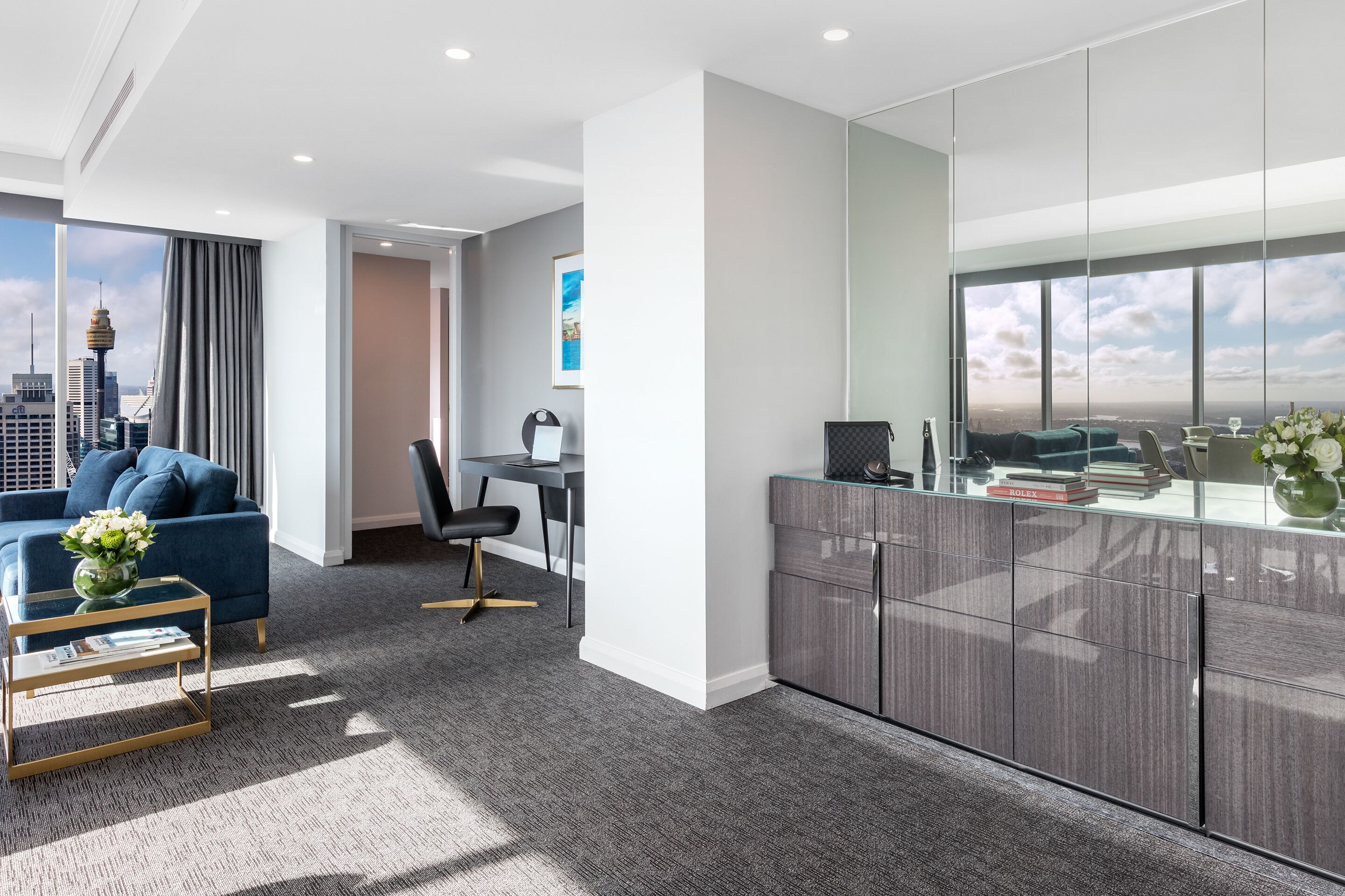 Una habitación de hotel moderna con vistas a la ciudad, un sofá azul, un escritorio y un espejo grande.