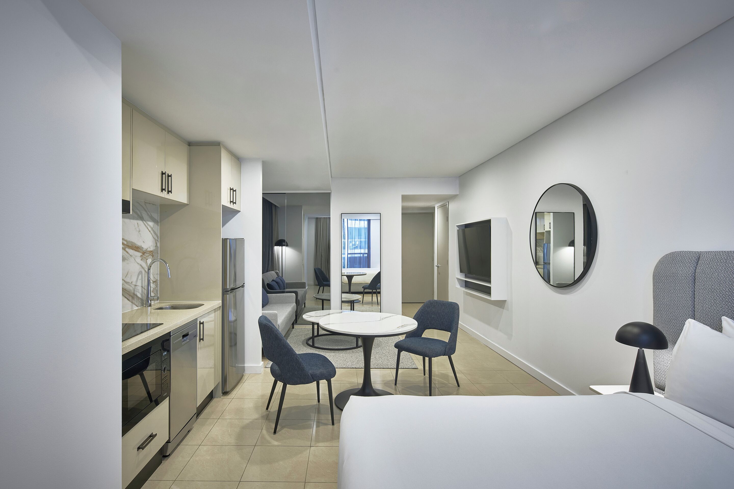 Una habitación de hotel moderna con cama, una mesa de comedor con sillas, una cocina y una sala de estar con sofá y televisor.