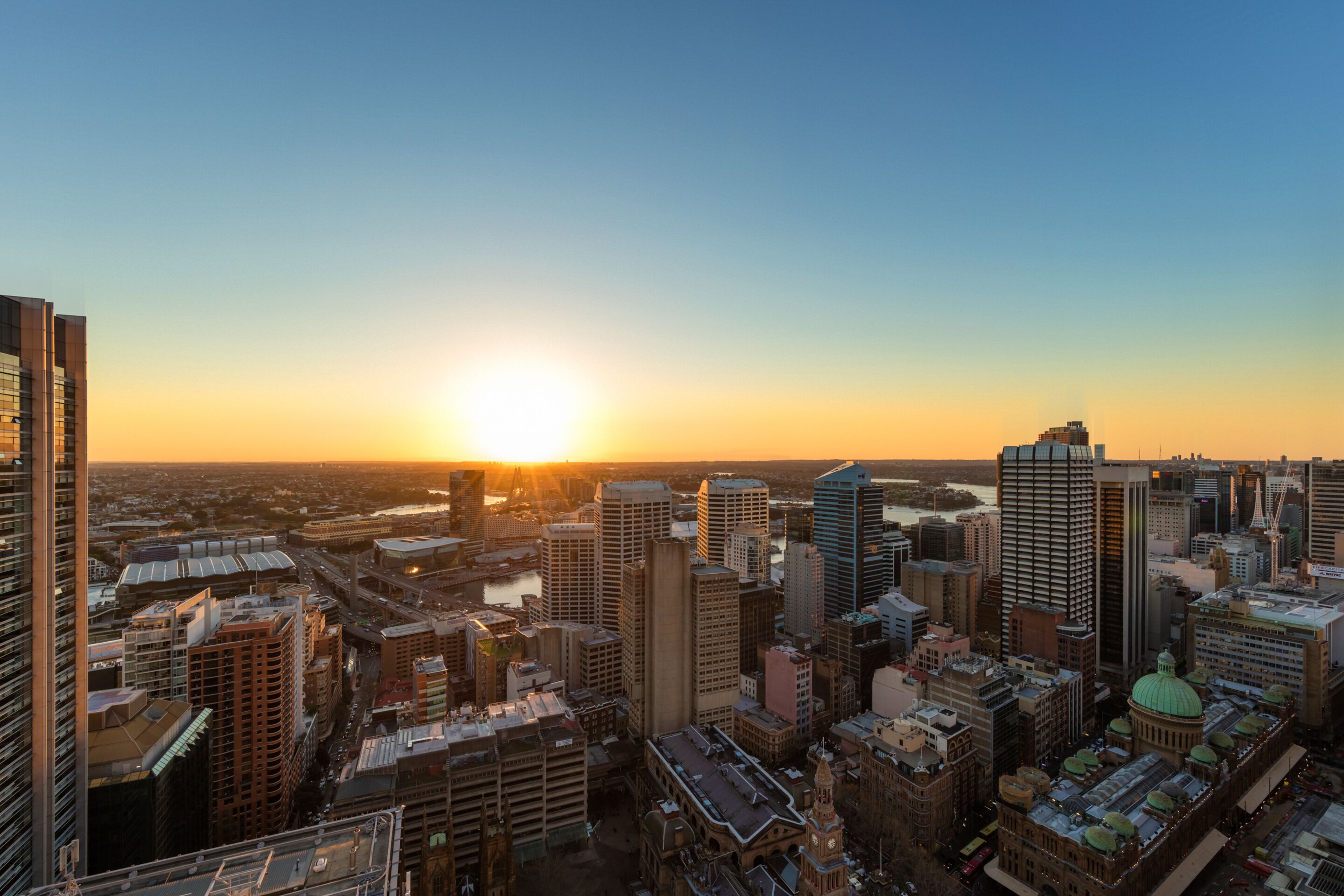 A cityscape at sunset with modern high-rise buildings and a historic building with a dome.