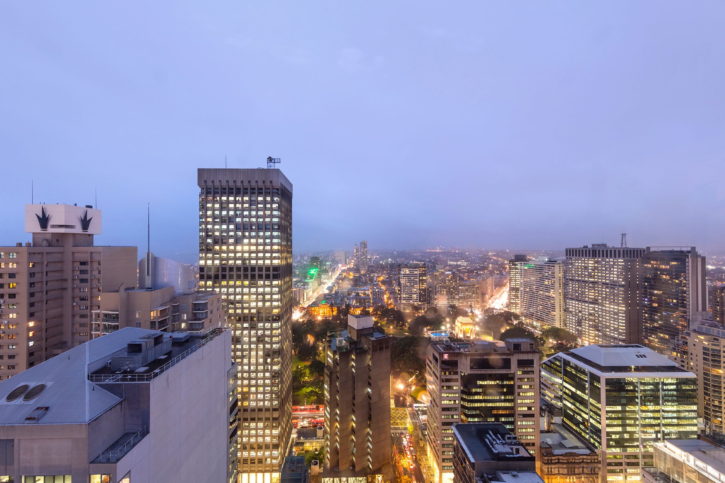 Un paysage urbain avec de hauts immeubles, une tour imposante au design original et une vue sur la ville au crépuscule.