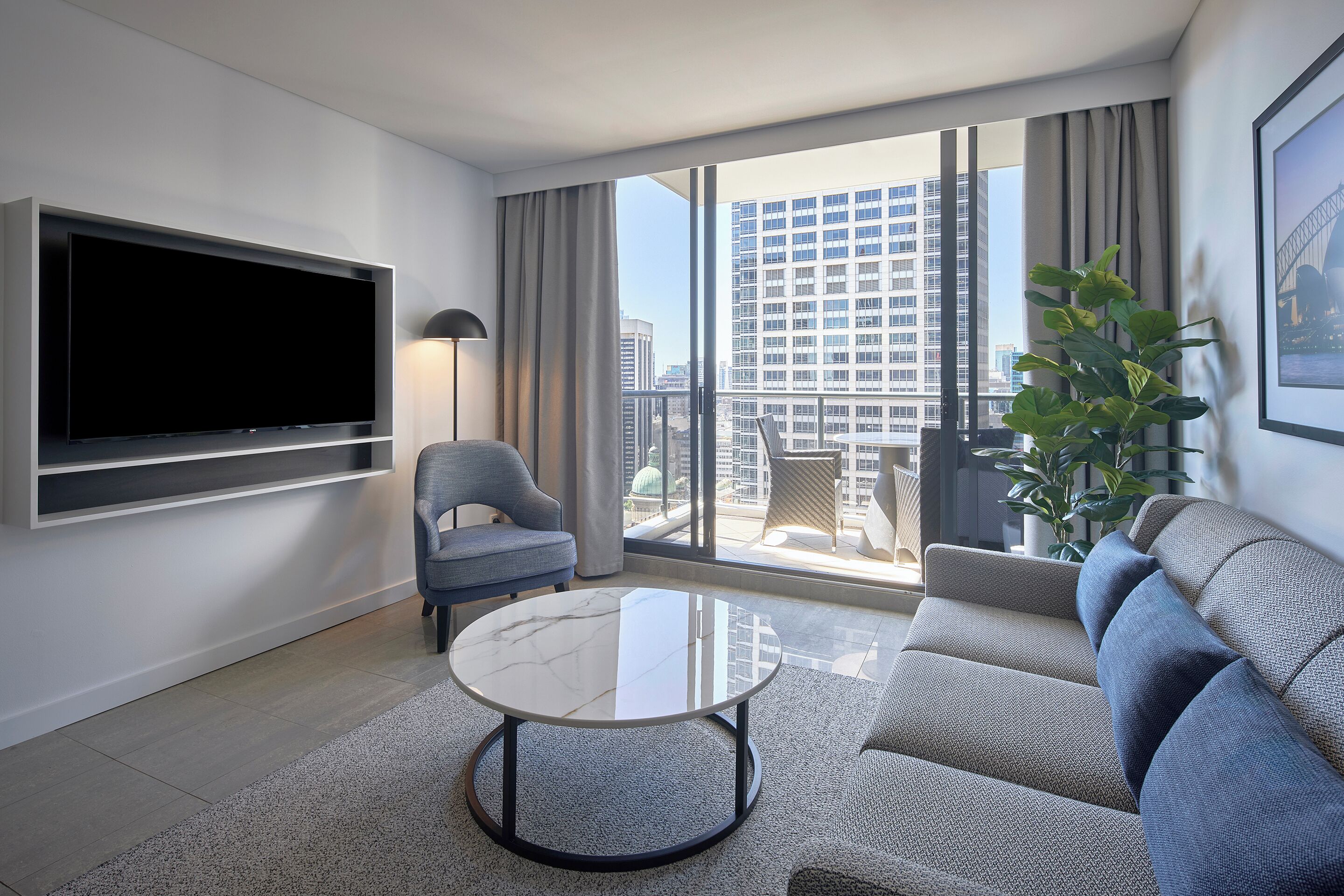 Een moderne woonkamer met een flatscreen-tv, een ronde salontafel, een bank, een fauteuil en een balkon met uitzicht op de stad.