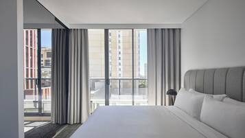 A modern hotel room with a large bed, a view of the city through floor-to-ceiling windows, and a balcony.