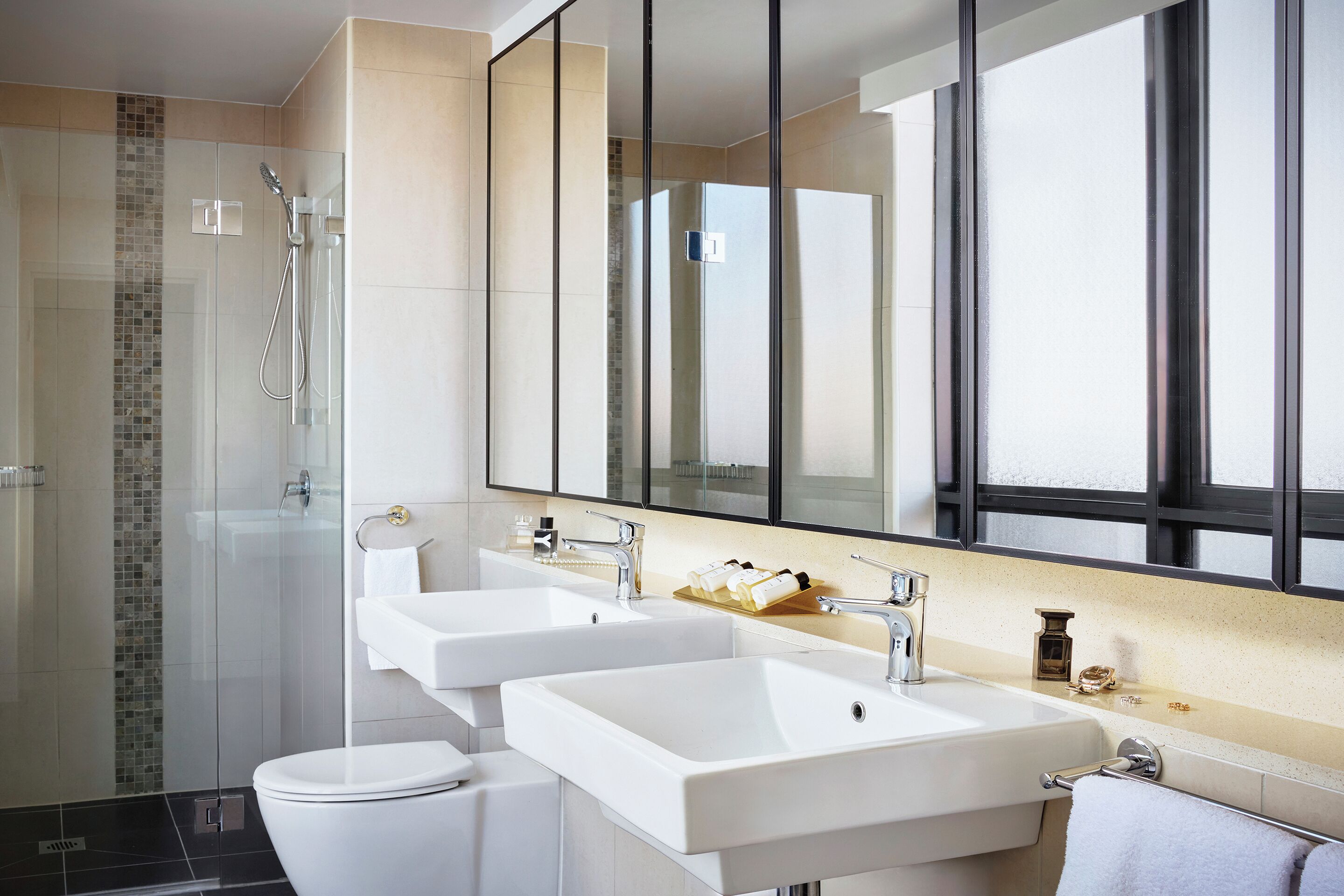 A modern bathroom with two sinks, a toilet, and a glass shower enclosure.