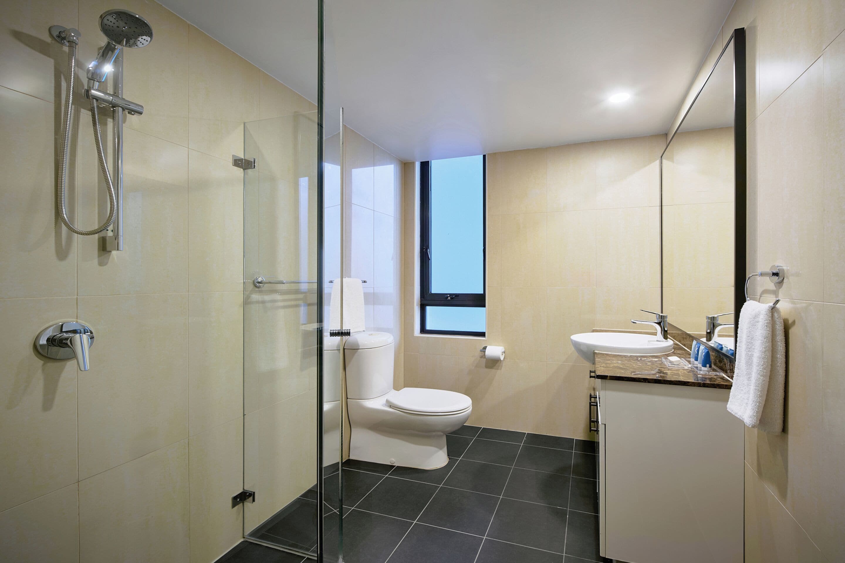 Une salle de bain moderne dotée d’une douche à parois de verre, de toilettes, d’un lavabo et d’une fenêtre laissant entrer la lumière naturelle.