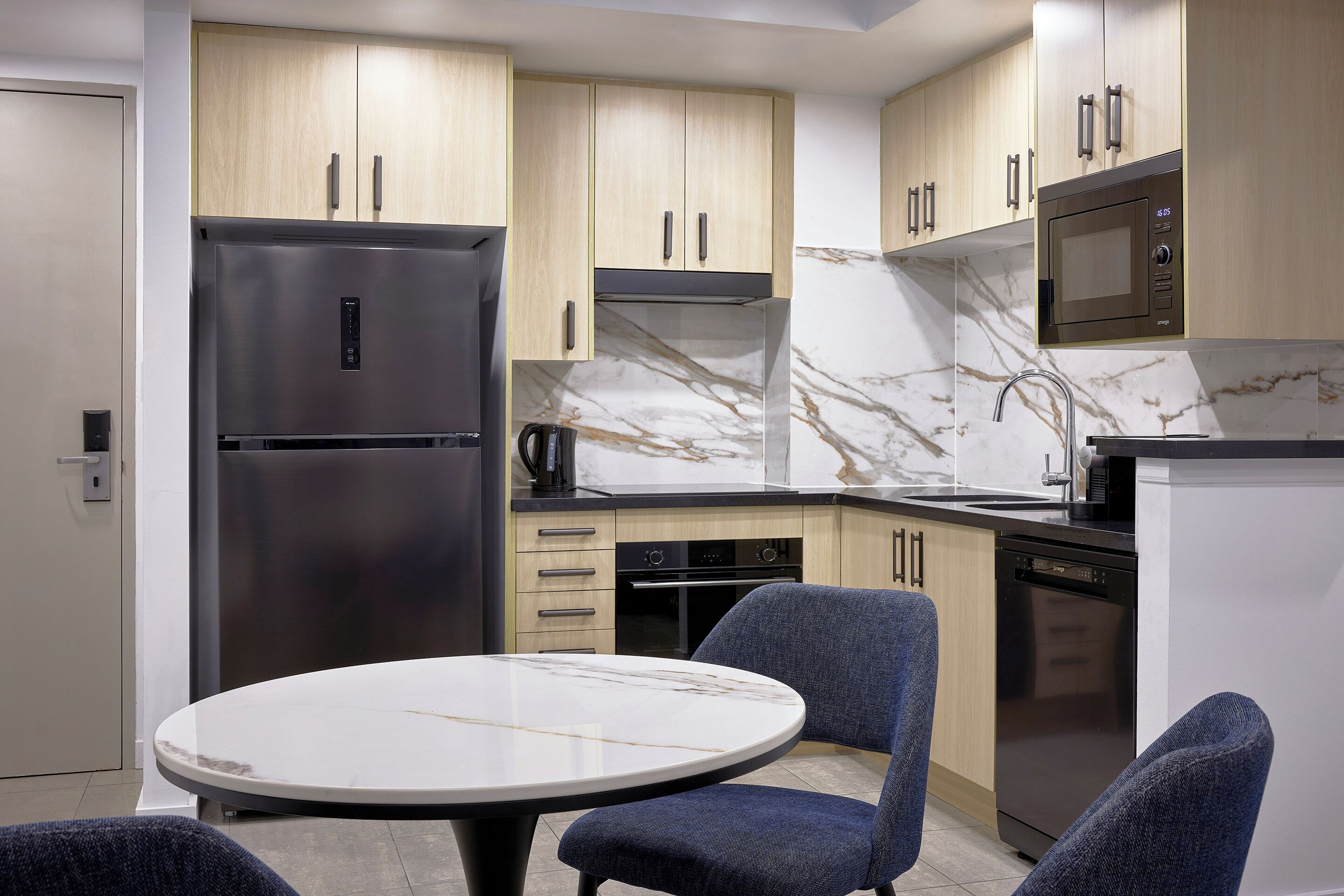 Een moderne keuken met een marmeren aanrecht, roestvrijstalen apparatuur en blauwe bekleden stoelen.