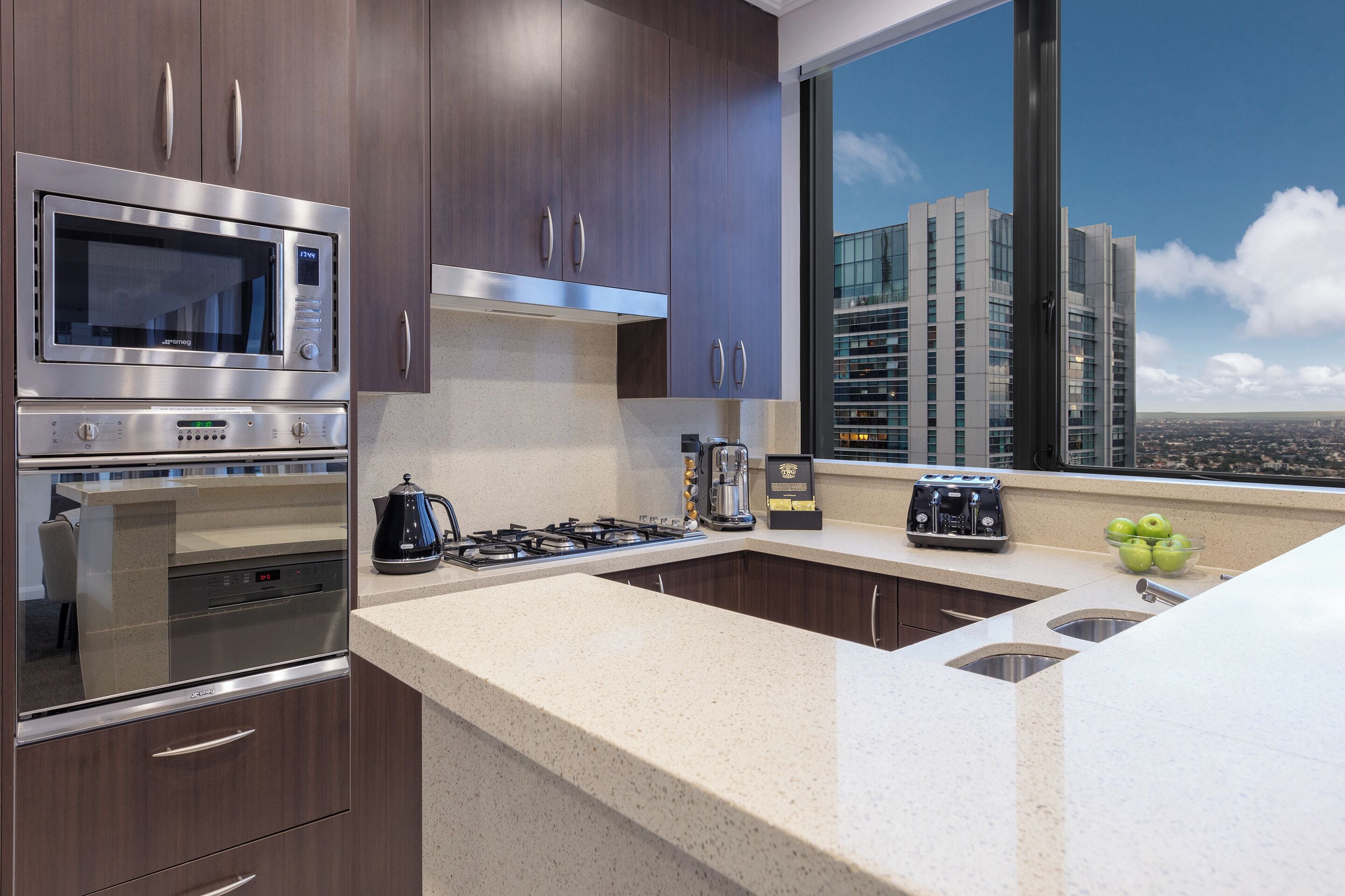 A modern kitchen with stainless steel appliances, a large window with a city view, and a countertop with a kettle and toaster.