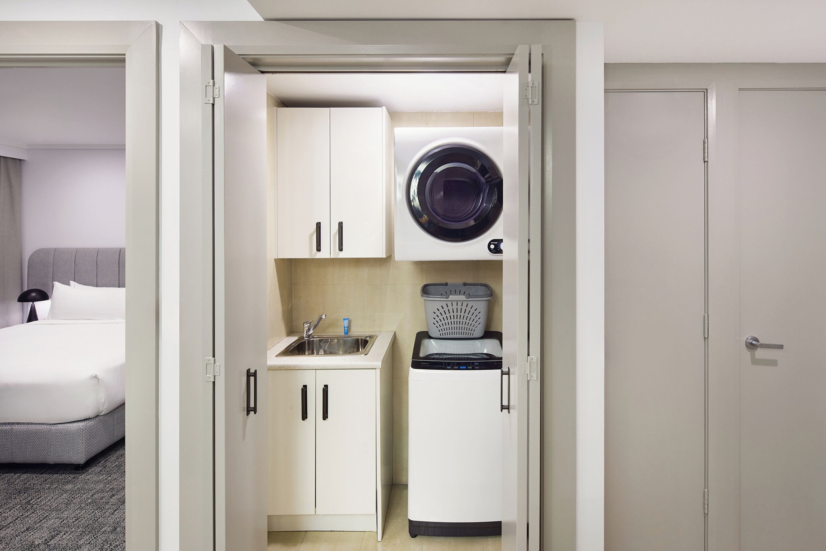 Une chambre d  ’hôtel compacte dotée d’une kitchenette, comprenant un évier, un petit réfrigérateur et un lave-linge.