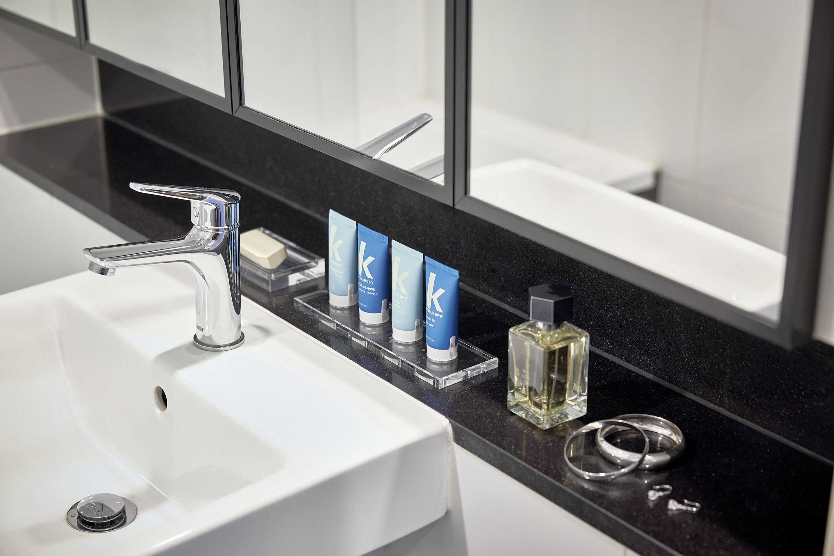 Un lavabo de salle de bain avec un robinet chromé, un miroir et un plan de toilette noir.