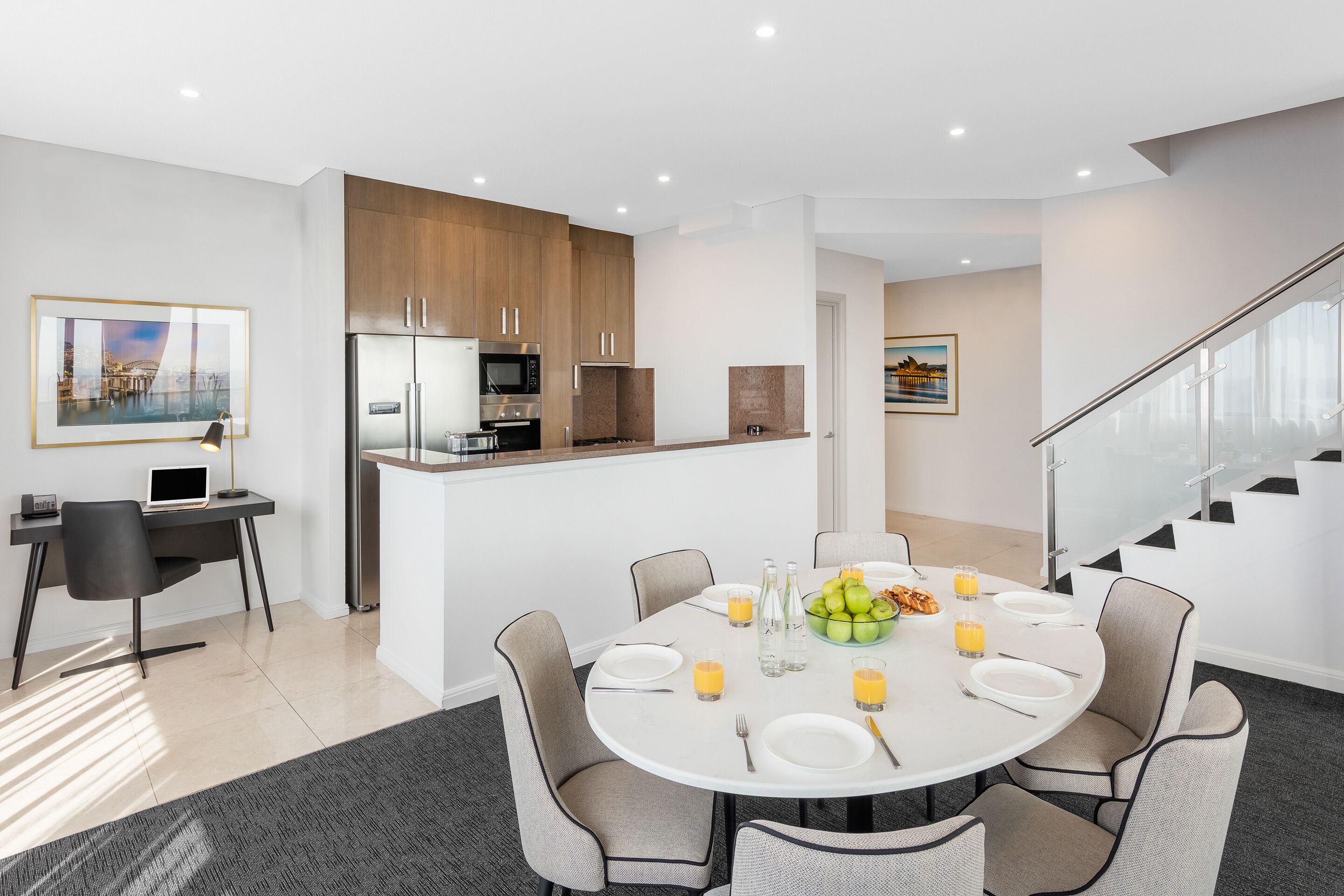 A modern kitchen with a dining area, featuring a round table with chairs, a refrigerator, a microwave, and a coffee machine.