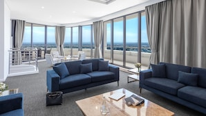 A spacious living room with two dark blue sofas, a coffee table, and a view of a cityscape through large windows. - Meriton Suites Kent Street, Sydney (Sydney)