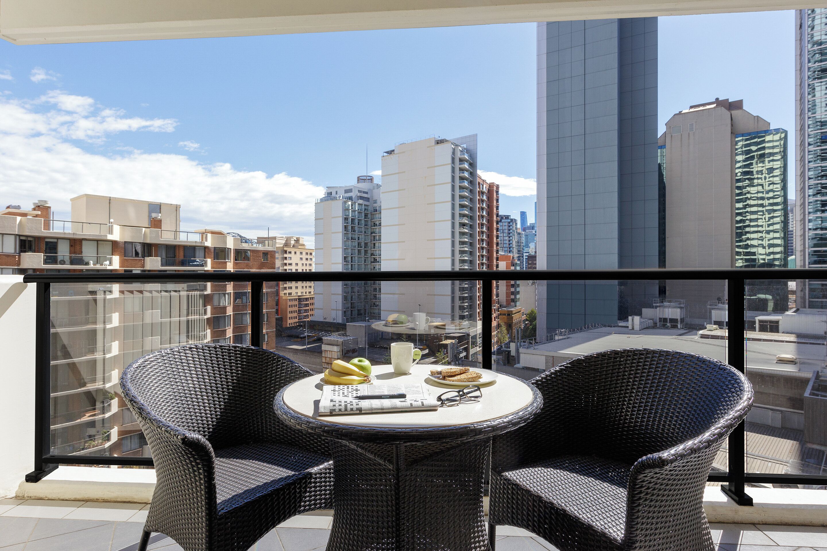 A balcony with wicker chairs, a table with food and drink, and a city view.