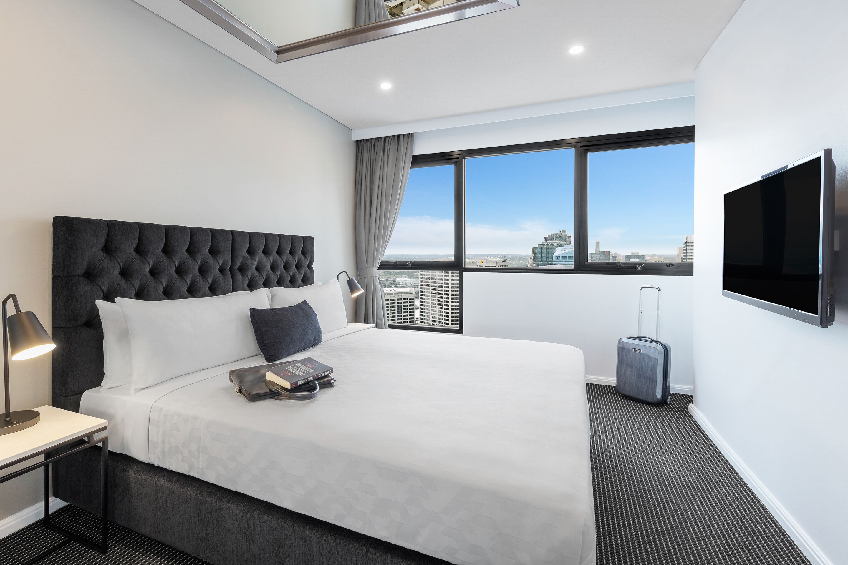 Habitación de hotel moderna con una cama grande, televisión de pantalla plana, maleta y vistas a la ciudad.