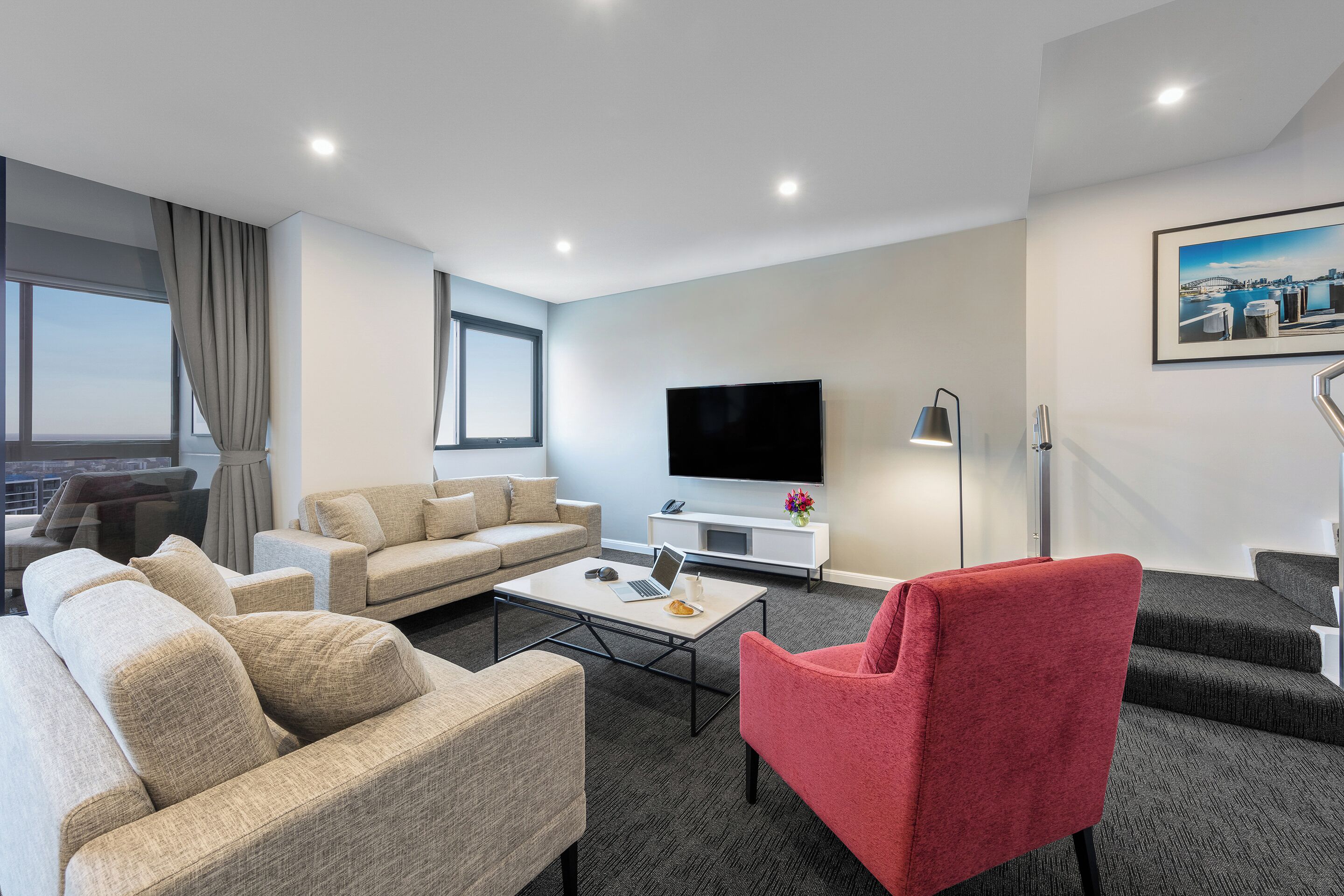 A modern living room with a flat-screen TV, a coffee table, and a red chair.