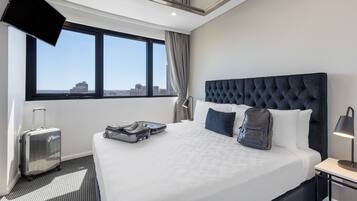 Una habitación de hotel con una cama grande, una maleta, una mochila y un televisor montado en la pared.